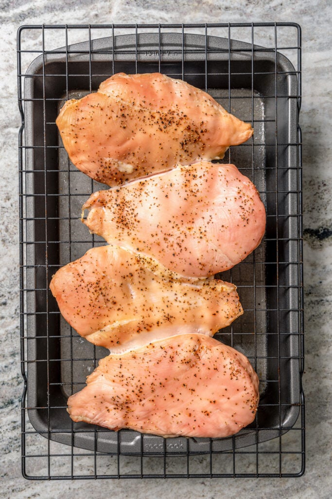 Placing the seasoned chicken breasts on the cooking rack over the pan. 