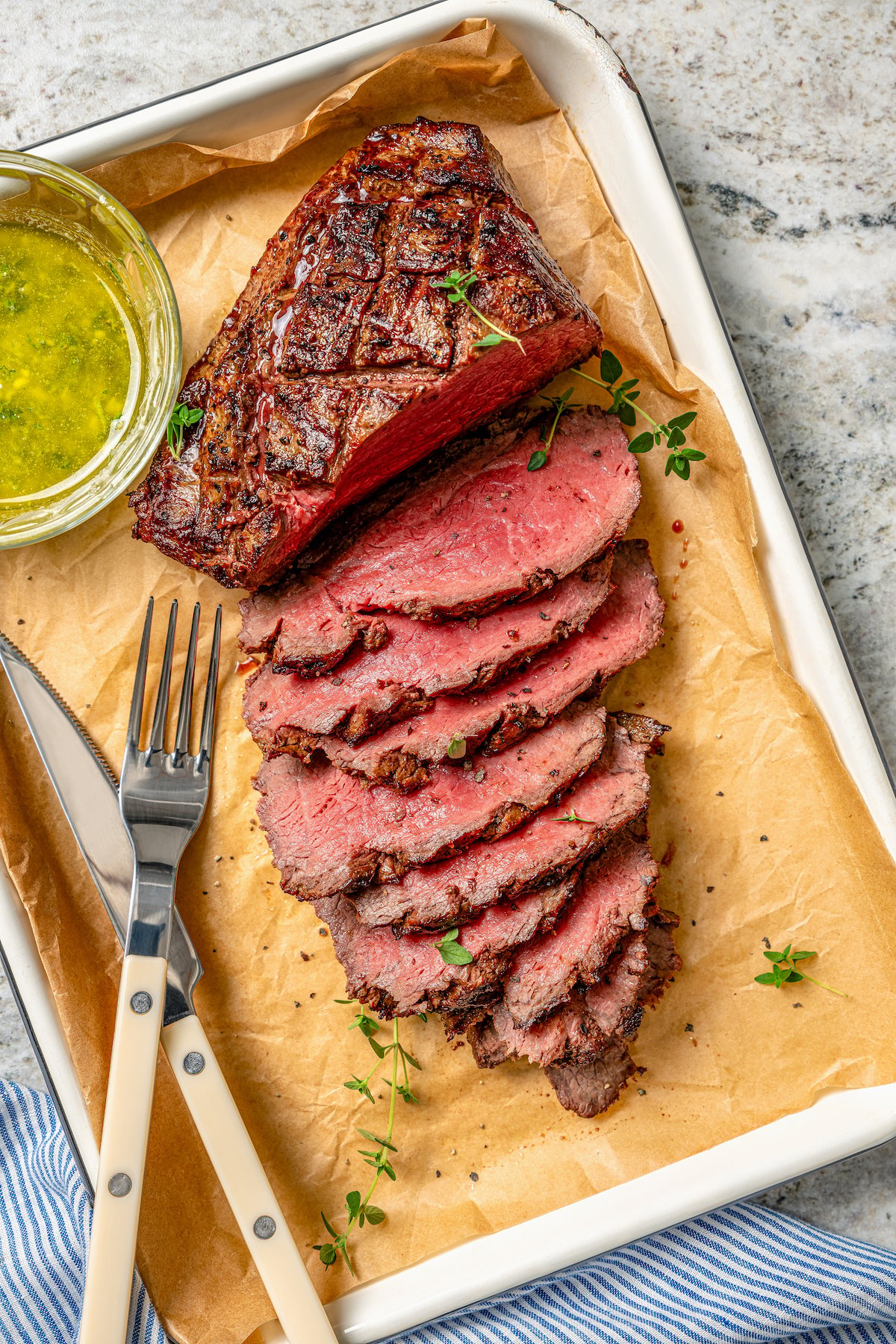 Sliced tri tip with a small bowl of herb sauce on the side. 