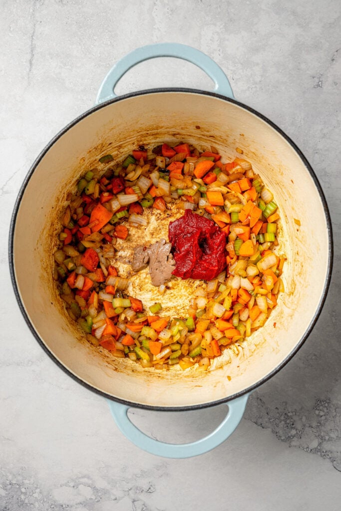 Adding the tomato paste and anchovy paste to the center of the Dutch oven. 