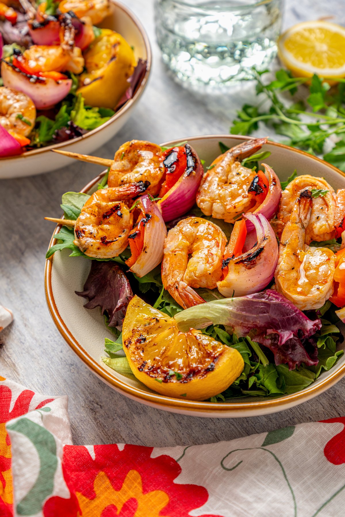 Bowl of salad with shrimp skewers and a grilled lemon. 